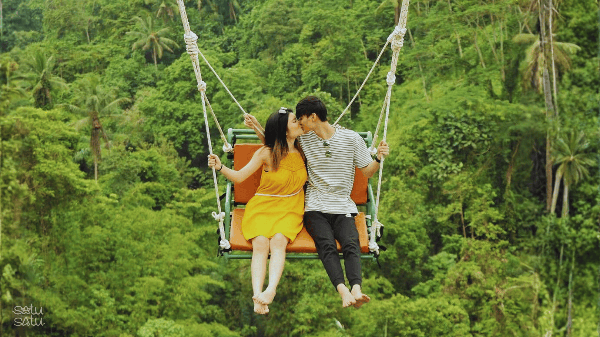 Couple enjoying Bali jungle swing Aloha Swing Ubud surrounded by lush tropical forest.