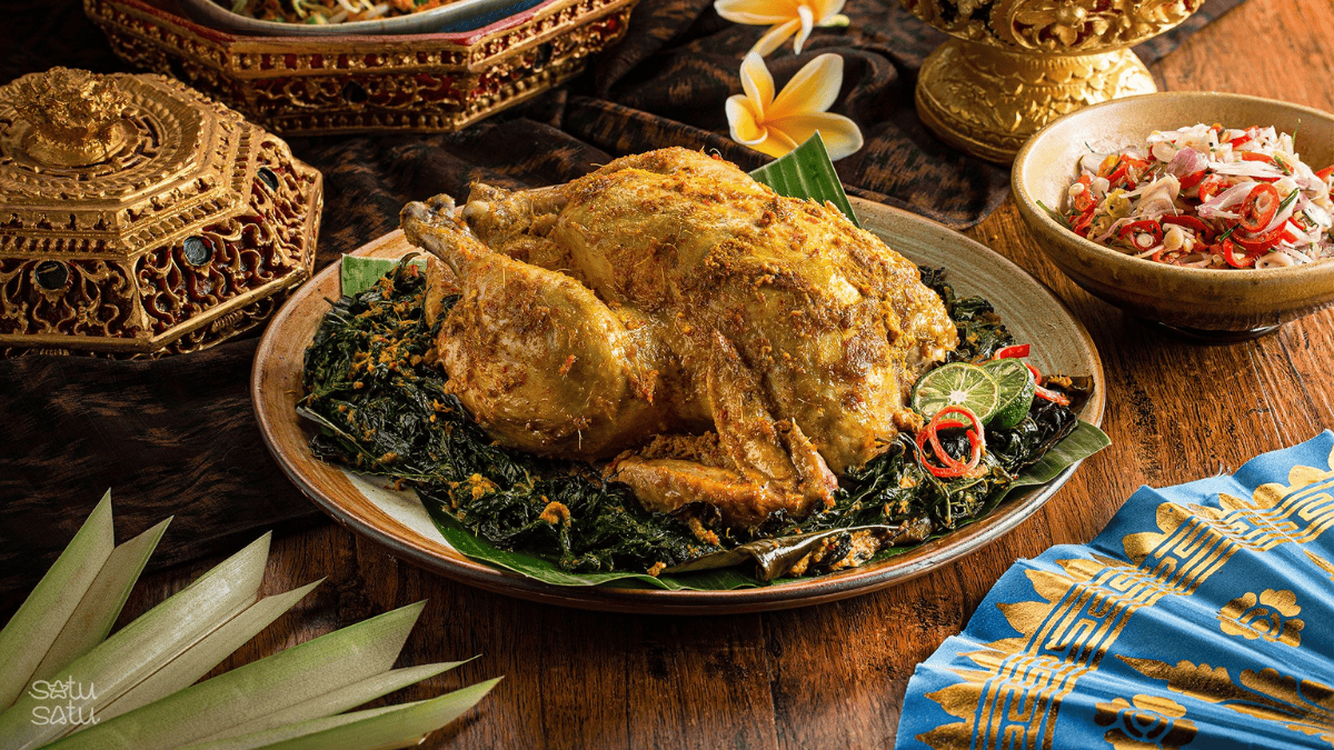 Traditional Balinese bebek betutu (spiced slow-cooked duck) served with vegetables and sambal on a wooden table in Bali, Indonesia.