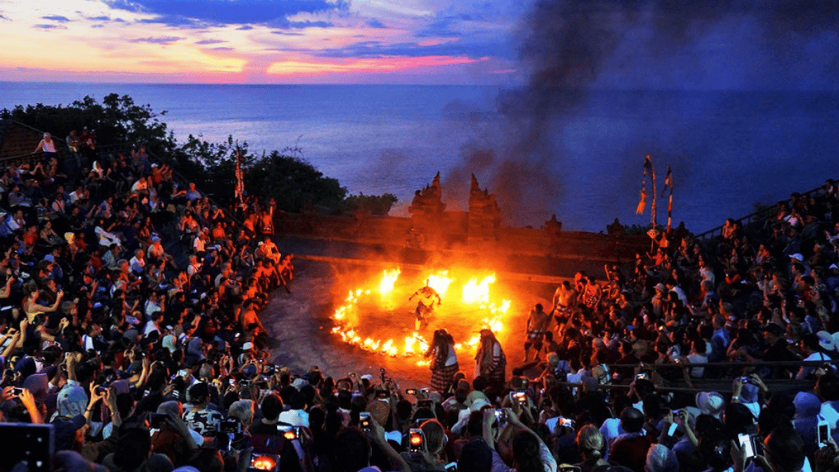 Kecak dance performance at Uluwatu Temple during sunset with fire and audience in Bali.