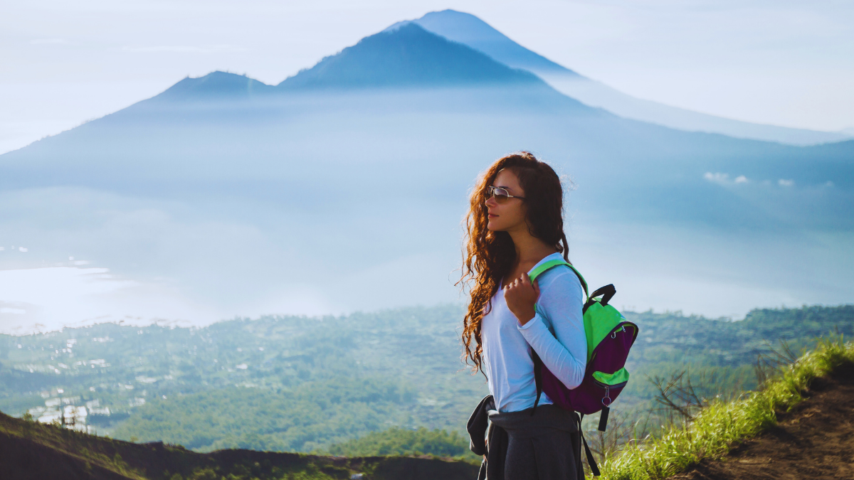 Female hiker standing at the summit of Mount Batur in Bali during sunrise with volcanic landscape in the background.