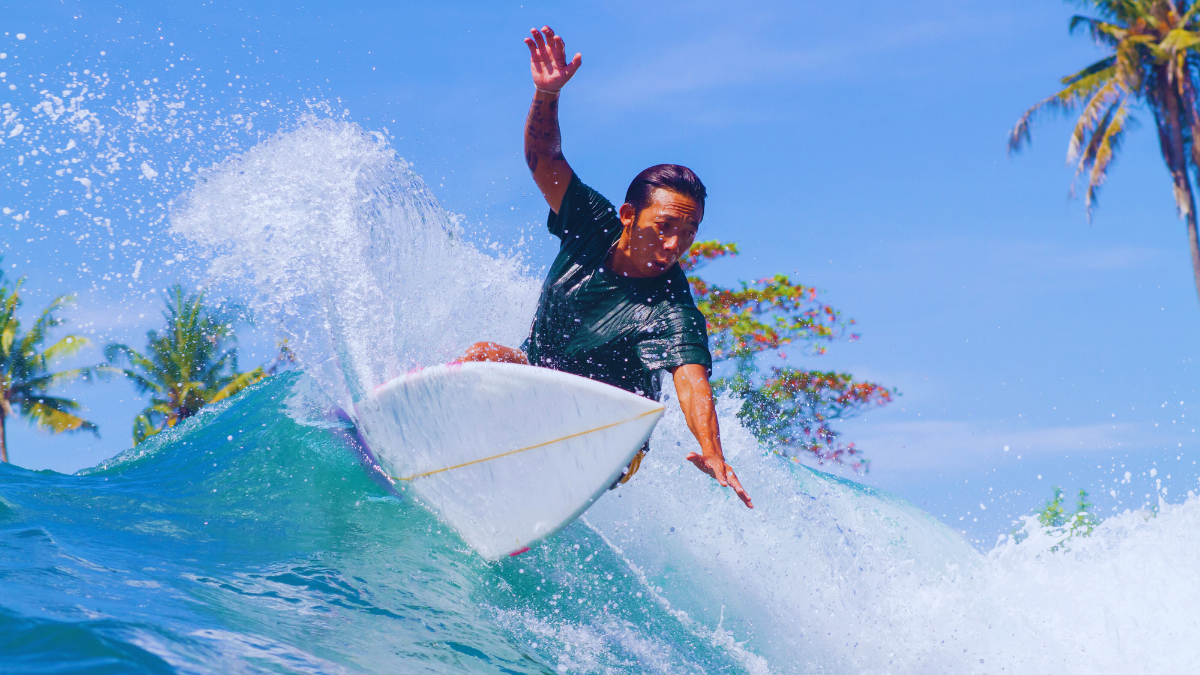 Surfer riding a wave in Bali with tropical scenery and palm trees in the background.