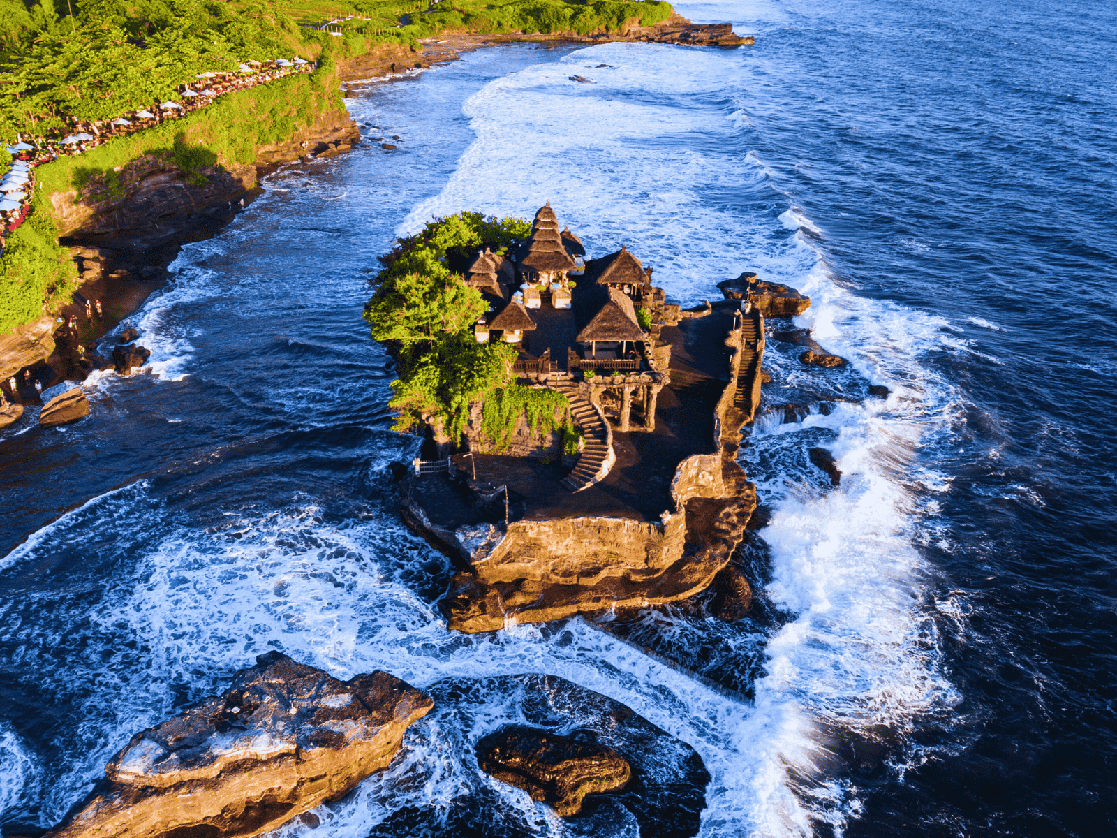 Bali Adventure Bucket List: Volcano Sunrises, Jungle Rivers, and Wild Island Escapes Aerial view of Tanah Lot Temple surrounded by ocean waves on Bali’s southwest coast.