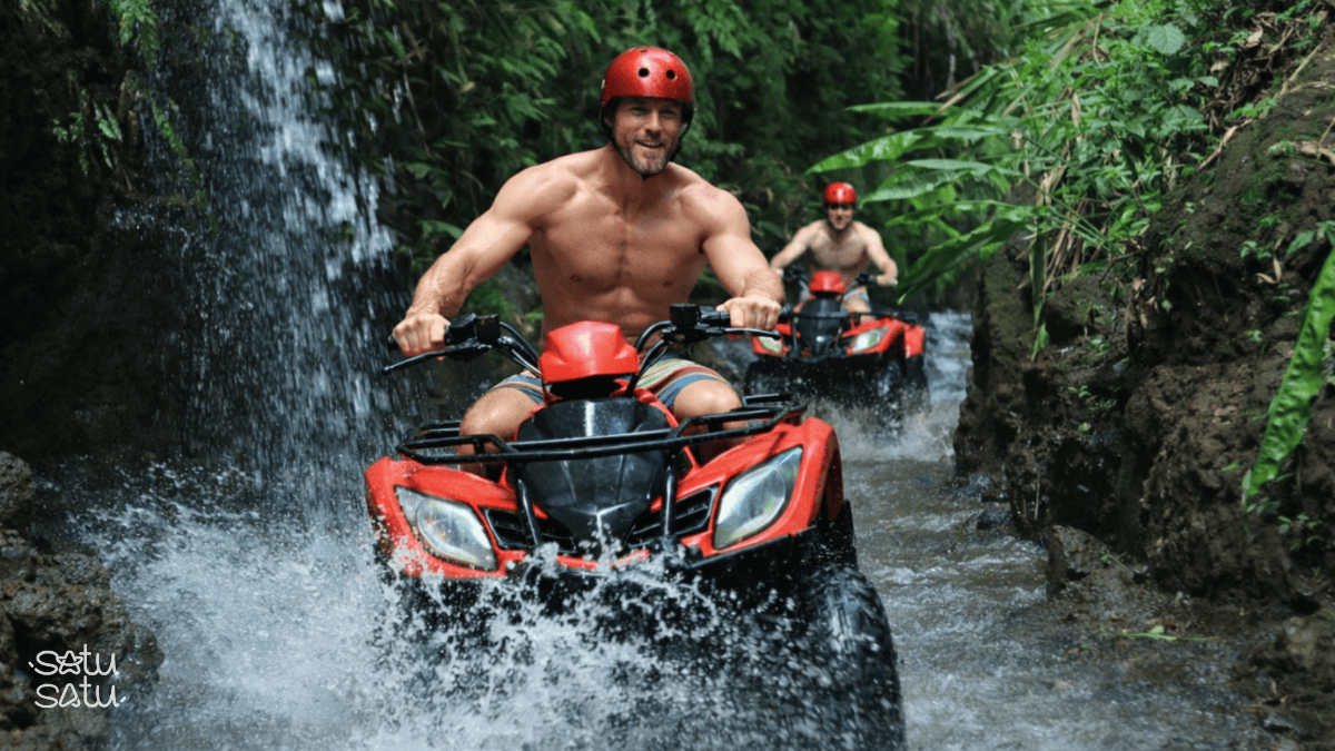 Adrenaline Lover Traveler riding an ATV through a jungle trail and shallow river in Ubud, Bali.