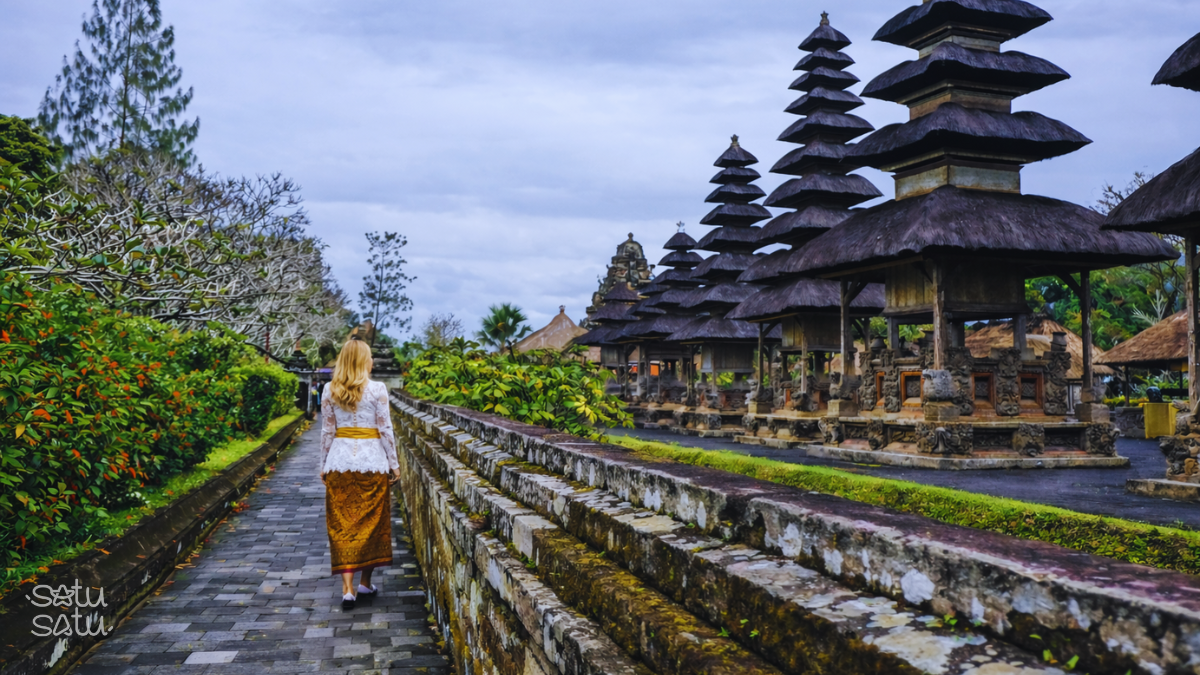 Traveler walking through Pura Taman Ayun in Mengwi Bali surrounded by traditional meru towers and lush gardens